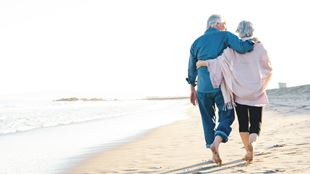 two older people walking on beach