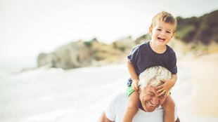 man carrying grandchild on shoulders on beach