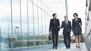 three business people walking over a glass footbridge