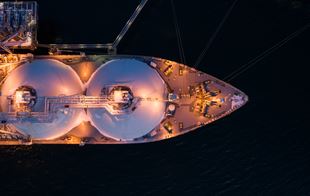 Top view of the front half of an illuminated  LNG tanker sailing at night