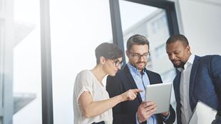 three people looking at tablet with sun shining in