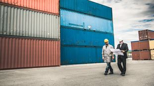 two men with map walking past shipping crates