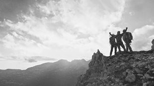 Three climbers celebrating at the top of a mountain watching the sunset