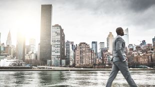 man walking past cityscape by the water