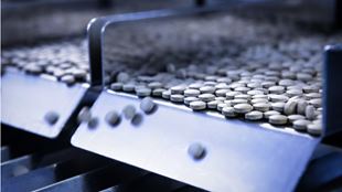 Round white pills moving through a chute onto a conveyor belt in a factory setting